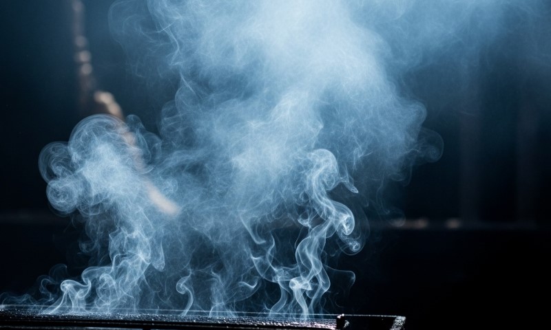 A person holds a cigarette in front of a cloud of smoke, creating a hazy atmosphere around them