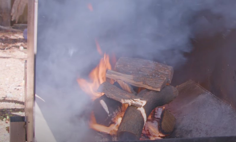 A fire burns brightly in a grill filled with wood