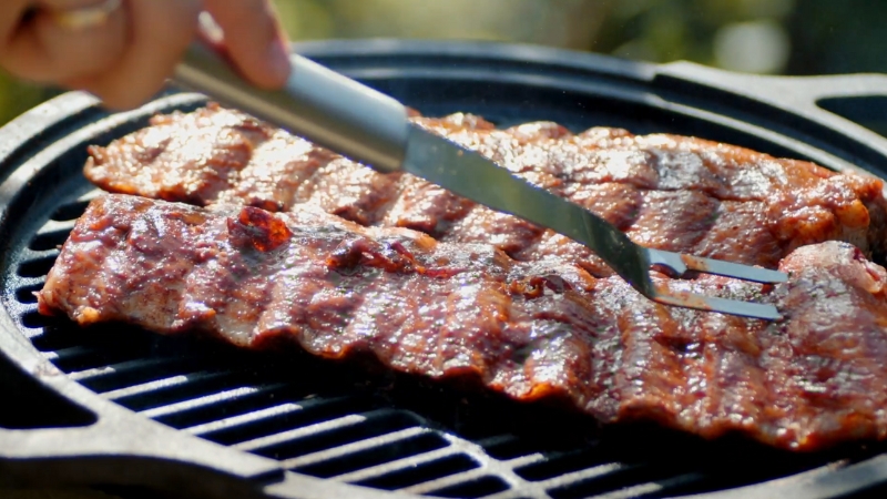 Wood combinations for smoking beef ribs shown on a grill with a fork lifting the meat