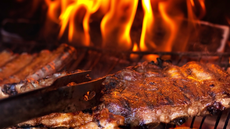 Beef ribs cook over open flames on a grill, showing a rich sear and smoky texture